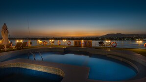 A pool area with lounge chairs and a lifebuoy, overlooking a body of water with city lights in the background. - Steigenberger Royale Nile Cruise - Every Thursday from Luxor for 07 & 04 Nights - Every Monday From Aswan for 03 Nights (Luxor)
