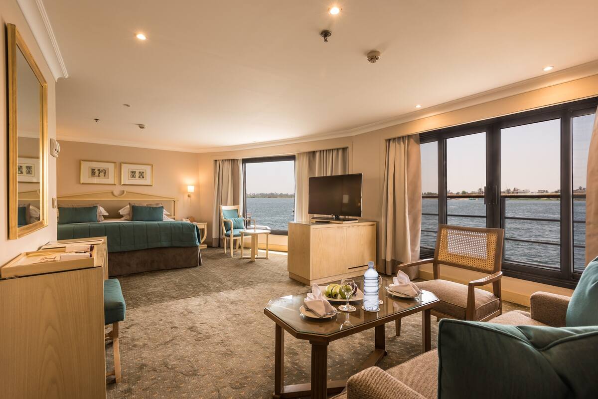 A hotel room with a bed, a desk, a chair, a TV, and a view of the water.
