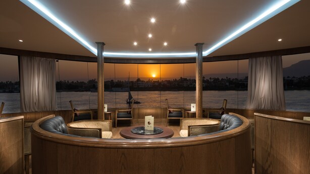 A luxurious interior with a central seating area, a wooden reception desk, and a view of the sunset over a body of water. - Steigenberger Royale Nile Cruise - Every Thursday from Luxor for 07 & 04 Nights - Every Monday From Aswan for 03 Nights (Luxor)