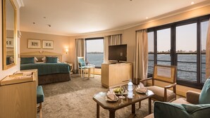 Quarto de hotel com cama, escrivaninha, televisão, cadeira e vista para a água.