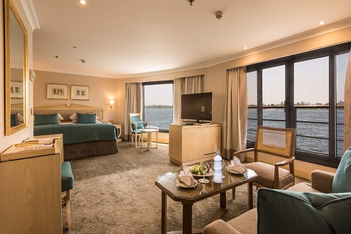A hotel room with a bed, a desk, a TV, a chair, and a view of the water.
