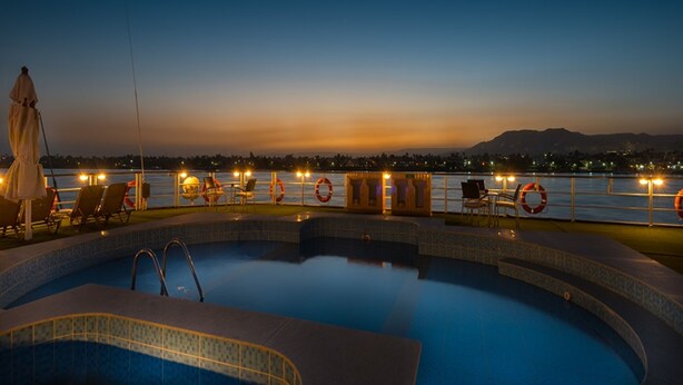 Área da piscina com espreguiçadeiras e vista para a água ao entardecer.