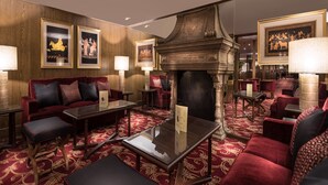 Um hall de hotel luxuoso com assentos estofados em vermelho, uma lareira imponente e obras de arte emolduradas nas paredes.