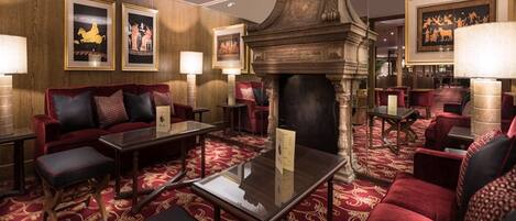 A luxurious hotel lobby with red upholstered seating, a grand fireplace, and framed artwork on the walls.