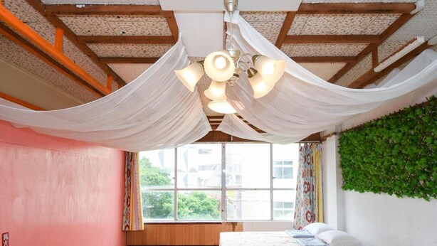 A room with a bed, a window with curtains, and a green wall with foliage. - Simple Stay Makishi (Naha)