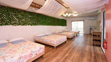 A hotel room with four beds, a green leafy wall, wooden flooring, and a shoe rack.