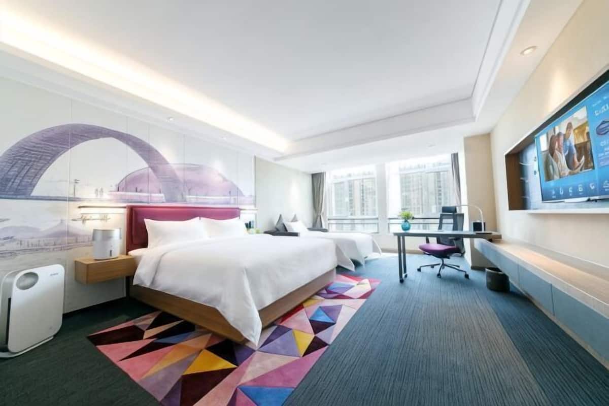 Una habitación de hotel con una cama grande, un escritorio, una silla, un televisor y una ventana con vista a la ciudad.