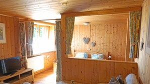 Interno di una baita in legno con divano, televisione e decorazioni a forma di cuore.