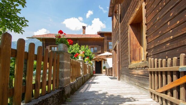 Un vialetto in legno conduce a un edificio con tetto rosso, circondato da una staccionata di legno e vasi di piante.