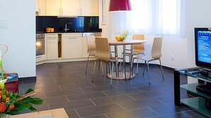 Une cuisine moderne avec des meubles blancs, un plan de travail noir et un luminaire suspendu rouge.