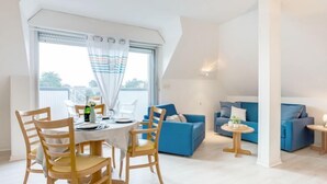 A modern living room with a dining area, featuring a round table, wooden chairs, a blue sofa, and a small side table. - Bleue Océane by Interhome (Carnac)