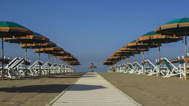Ein Strand mit Reihen von gestreiften Sonnenschirmen und weißen Liegestühlen.