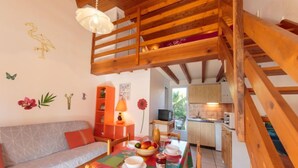 Un interior acogedor con una escalera de madera, una zona de comedor con mantel colorido y una cocina con armarios de madera.