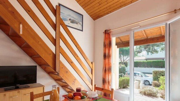 Un comedor con una mesa dispuesta para dos, un televisor en un mueble y una ventana con cortinas.