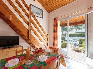 A dining area with a table set for two, a television on a cabinet, and a window with curtains. - Vacation home Marais by Interhome (Vaux Sur Mer)