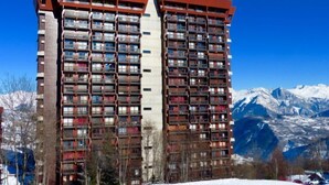 Un hôtel de grande hauteur doté de nombreux balcons, situé au pied d’une montagne enneigée.