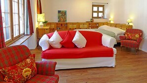 Une pièce chaleureuse avec un canapé rouge, un fauteuil assorti, un lit en bois avec deux oreillers et une table de chevet avec une lampe.