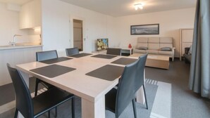 A modern living room with a large dining table, several chairs, a sofa, and a small kitchen area. - Strandhuis with balcony by Interhome (Bredene)