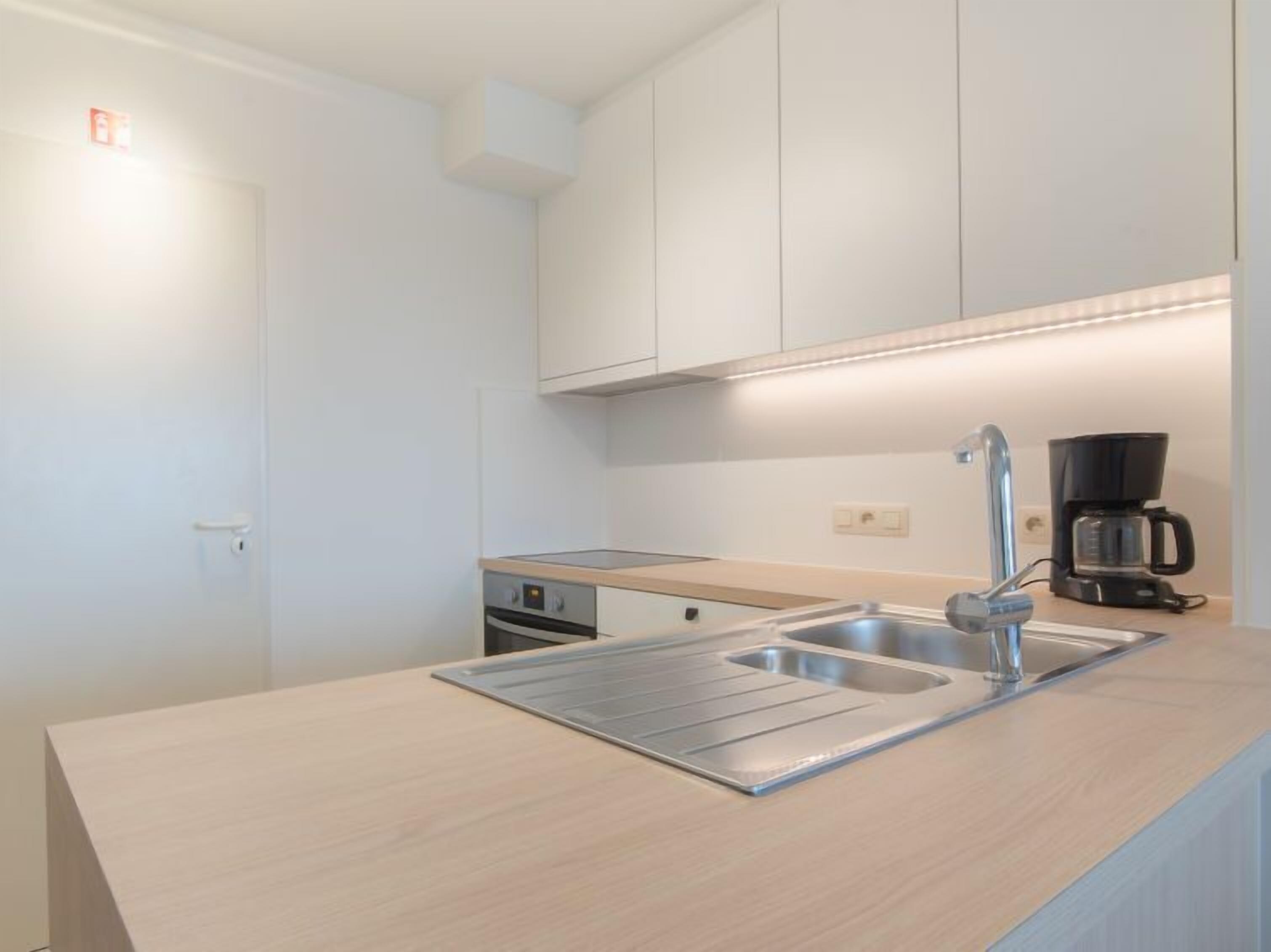 Een moderne keuken met een roestvrijstalen spoelbak, een koffiezetapparaat en witte kasten.