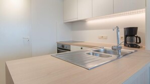 A modern kitchen with a stainless steel sink, a coffee maker, and white cabinetry. - Strandhuis with balcony by Interhome (Bredene)