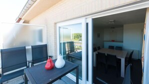 An outdoor patio with a table and chairs, a red and white vase, and a glass door leading to an interior dining area. - Strandhuis with balcony by Interhome (Bredene)