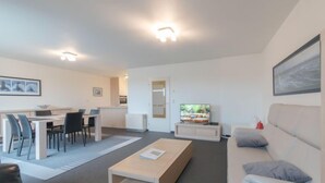 A modern living room with a sofa, a coffee table, a TV, and a dining area with chairs and a table. - Strandhuis with balcony by Interhome (Bredene)