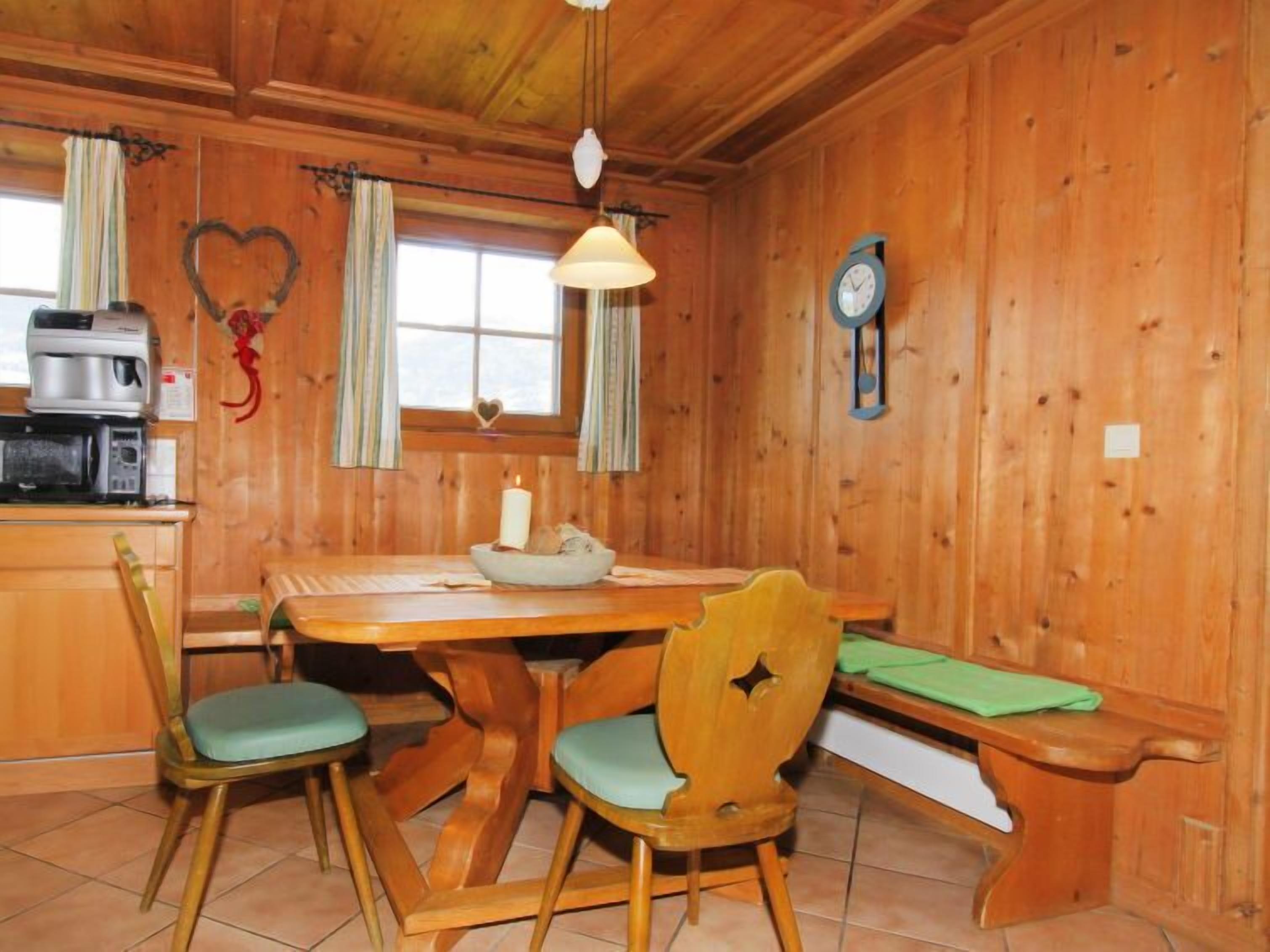 Ein Holzinterieur mit einem Esstisch, Stühlen, einer Bank, einer Uhr und einer wandmontierten Kaffeemaschine.