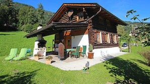 A traditional wooden chalet with a sloped roof, a porch with outdoor seating, and a well-maintained lawn. - Auhäusl by Interhome (Fügen)
