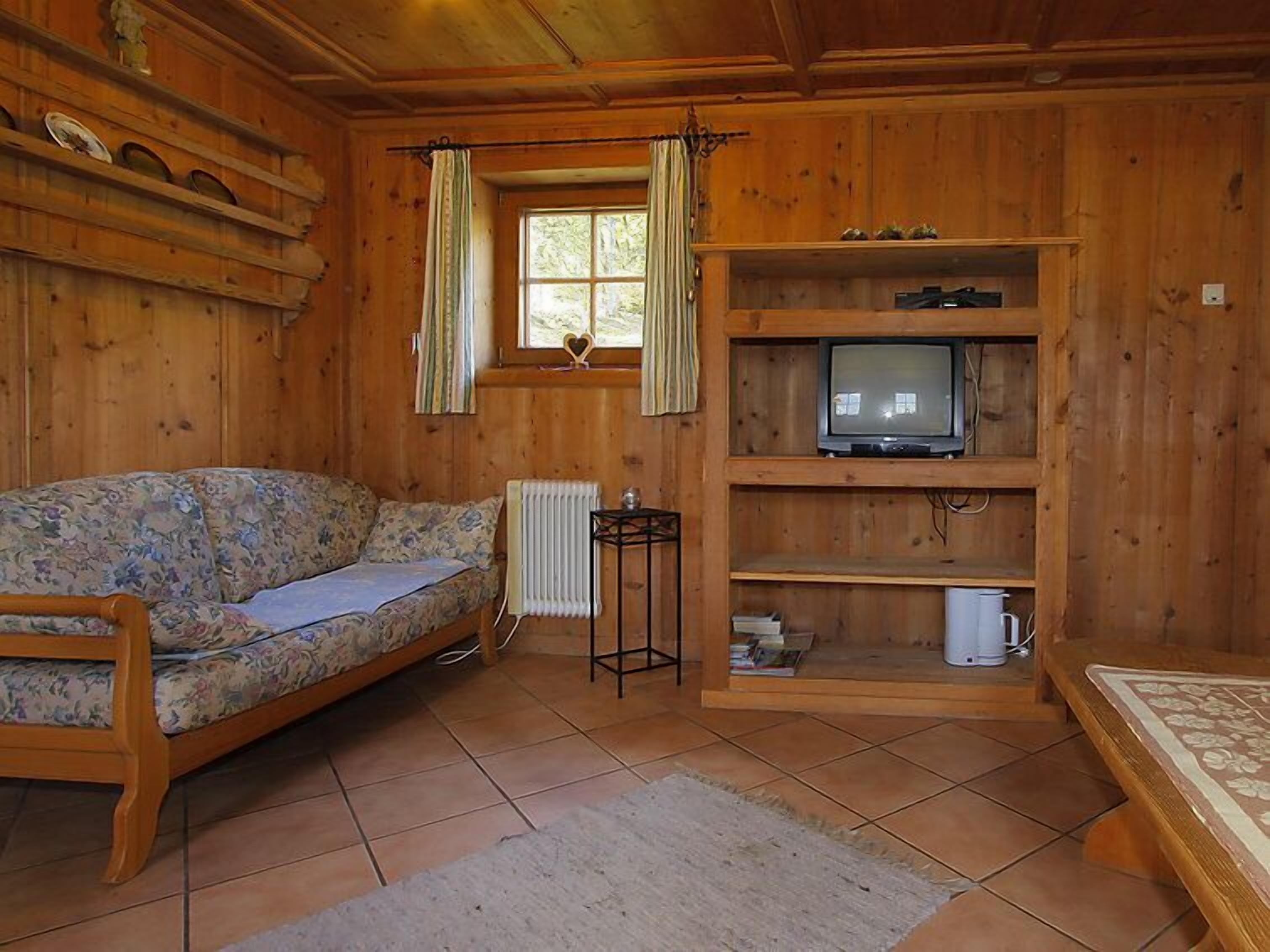 Ein Holzblockbau-Innenraum mit einer Couch, einem Fernseher auf einem Regal und einem Fenster mit Vorhängen.