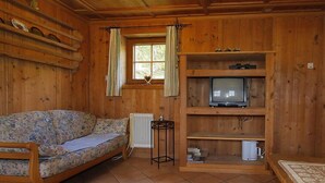 A wooden cabin interior with a sofa, a television on a shelf, and a window with curtains. - Auhäusl by Interhome (Fügen)