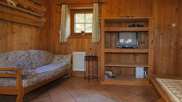 Ein Holzblockbau-Innenraum mit einer Couch, einem Fernseher auf einem Regal und einem Fenster mit Vorhängen.