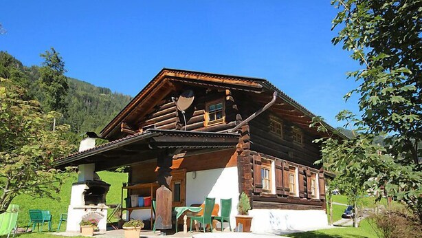 A traditional wooden house with a stone bench in the foreground, surrounded by greenery and a clear blue sky. - Auhäusl by Interhome (Fügen)