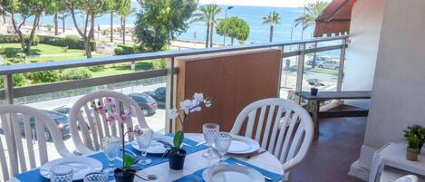 A dining table set with white chairs, plates, and cutlery, overlooking a scenic view of the sea and greenery.