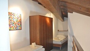 Une petite chambre accueillante, avec deux lits simples, une armoire en bois et un tableau abstrait aux couleurs vives accroché au mur.