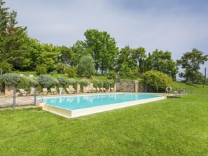 Una piscina rectangular con un muro de piedra y un césped.