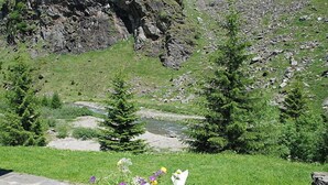 Ein Steintisch mit floraler Dekoration und einem Teller mit Gabel, vor einer Berglandschaft mit Fluss.