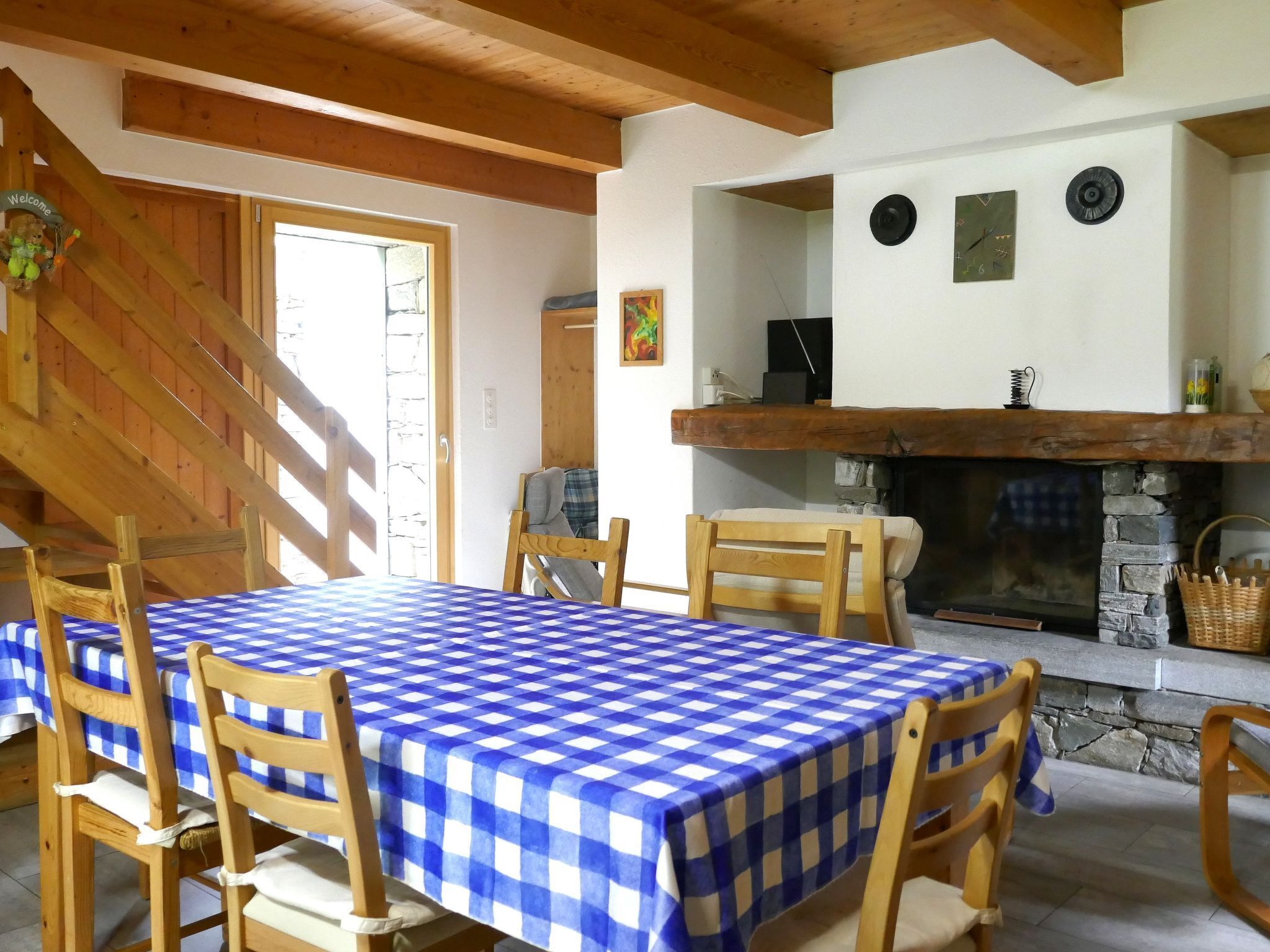 Uma sala de jantar com toalha xadrez, cadeiras de madeira, lareira e escada de madeira.