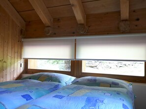 Een houten kamer met twee bedden, elk met een gewatteerde spreideken, en een raam dat uitzicht biedt op een rotsachtig landschap.