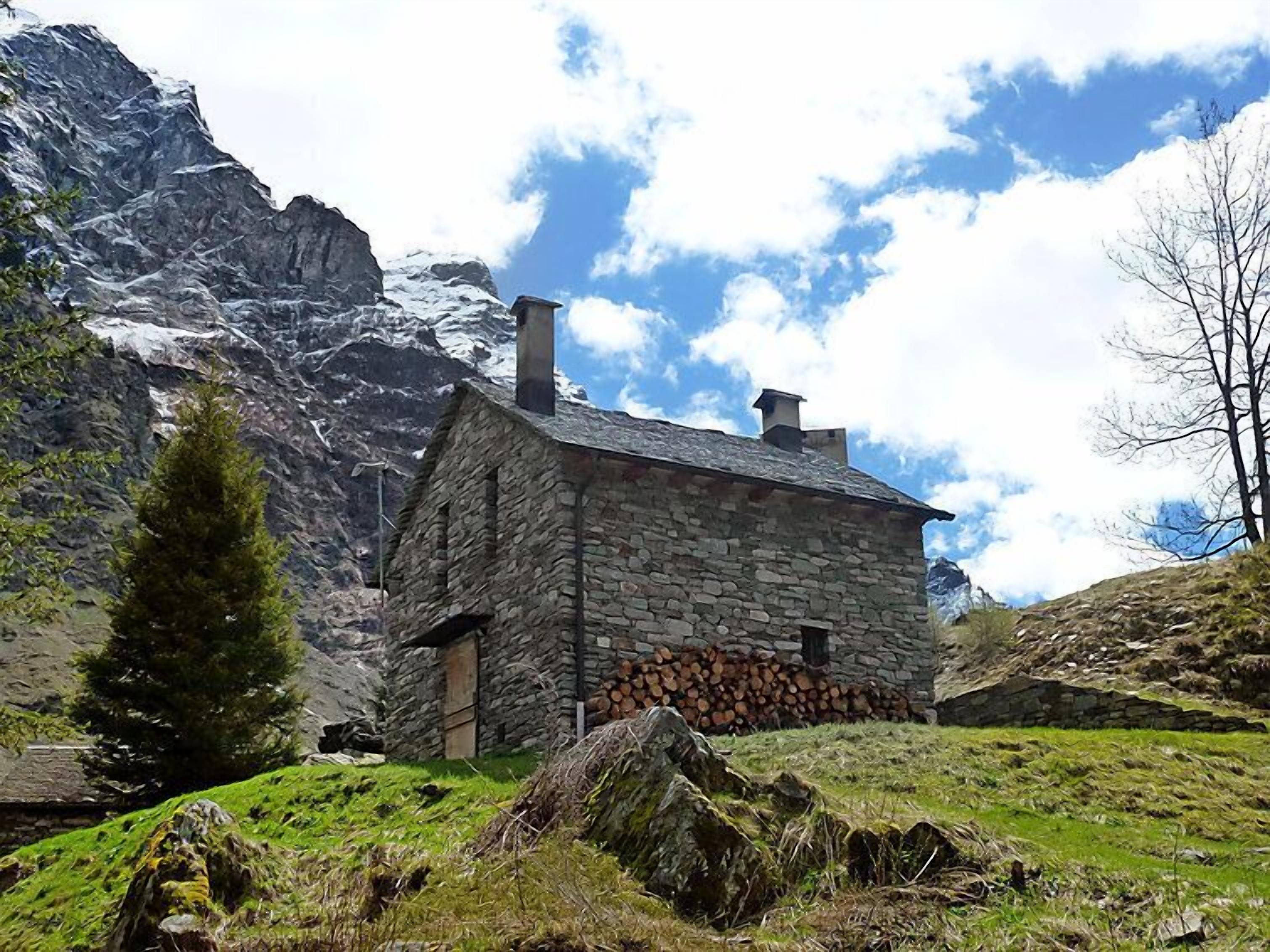 A stone house with a sloped roof, surrounded by a mountainous landscape and a clear sky.