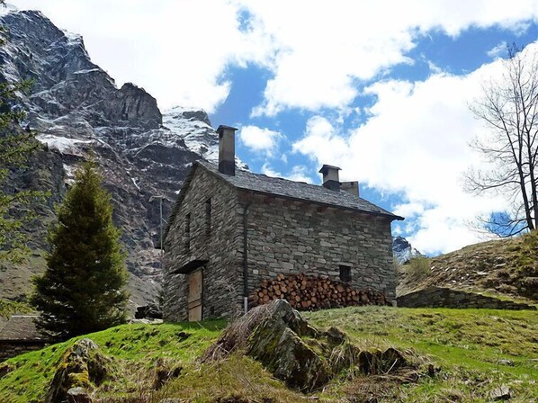 Ein Steinhaus mit geneigtem Dach, eingebettet in eine gebirgige Landschaft unter klarem Himmel.