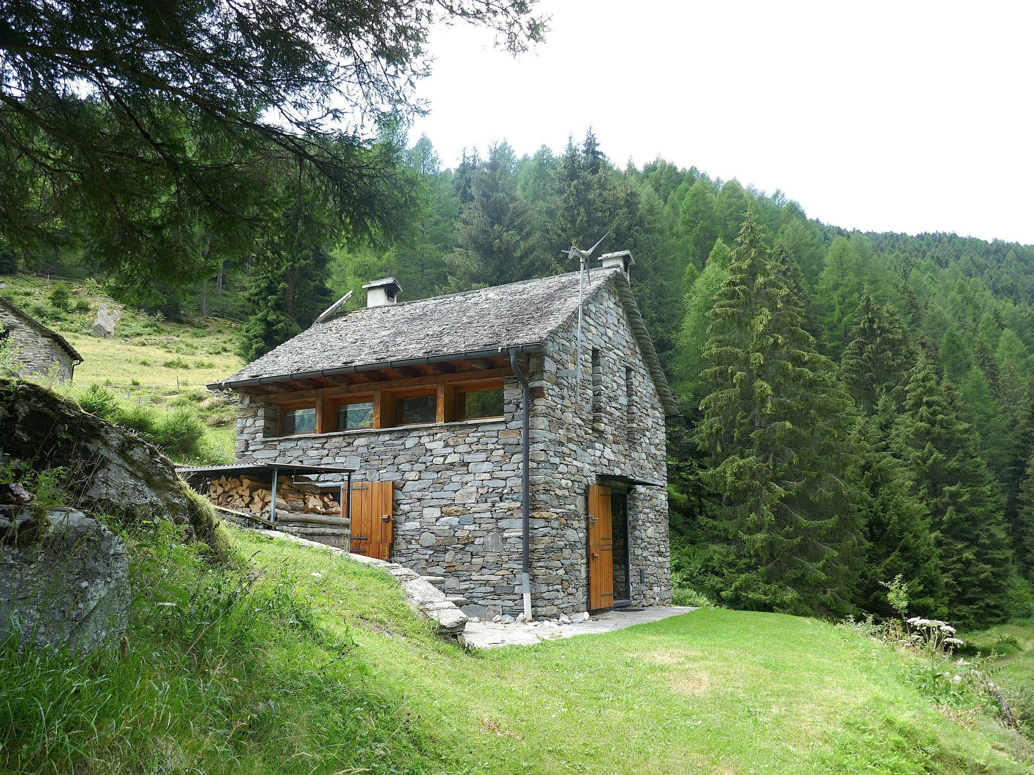 A stone house with a sloped roof, wooden doors, and a small porch area.