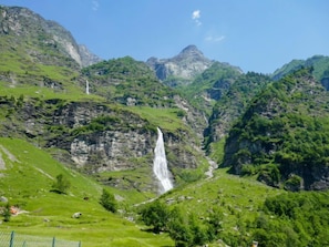 Eine gebirgige Landschaft mit einem Wasserfall, üppigem Grün und felsigen Klippen.