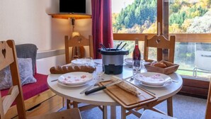 A dining area with a table set for two, a television above the table, and a scenic view through the window. - Vostok Zodiaque by Interhome (Le Corbier)