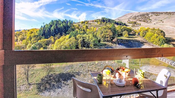 A dining area with a table set for two, overlooking a scenic landscape with trees and hills. - Vostok Zodiaque by Interhome (Le Corbier)