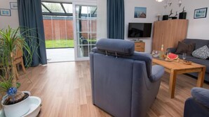 Uma sala de estar moderna com um sofá, uma mesa de centro, uma TV e uma porta de vidro deslizante que dá para um jardim.