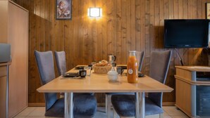 Ruokailutilassa on puinen seinä, televisio sekä pöytä, joka on katettu leivällä, kannulla ja kupilla.