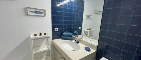 Ein modernes Badezimmer mit einem weißen Waschbecken, blauen Fliesen, einem Spiegel und einer kleinen Ablage mit Pflanzen.