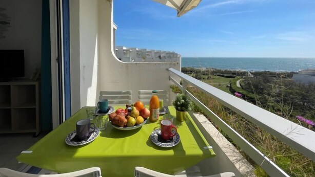 A balcony with a table set for breakfast, overlooking a coastal view.