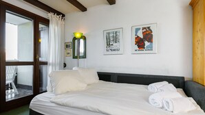 Hotellihuone, jossa on sänky, tuoli ja kaksi kehystettyä kuvaa seinällä.