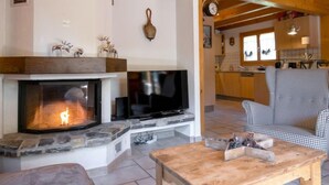 A cozy living room with a stone fireplace, a flat-screen TV, and a checkered sofa. - Miranda by Interhome (Champex)